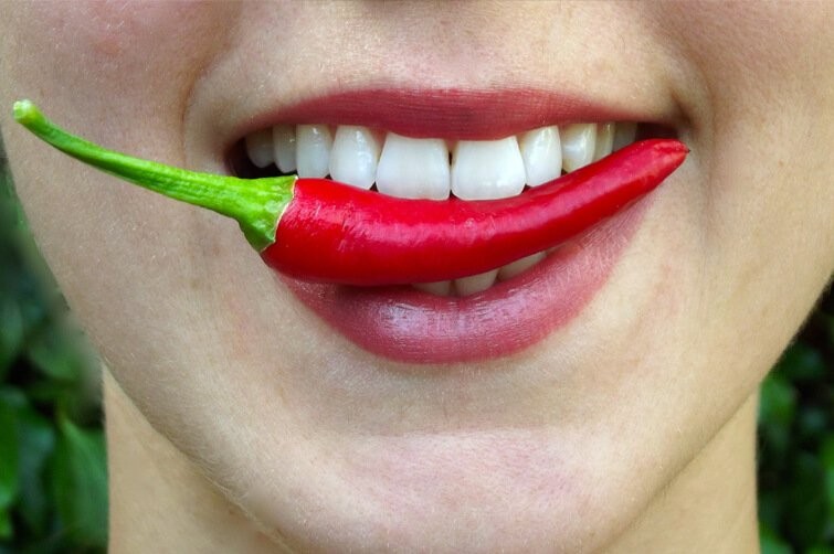 Uśmiechnięta dziewczyna z papryczką w zębach